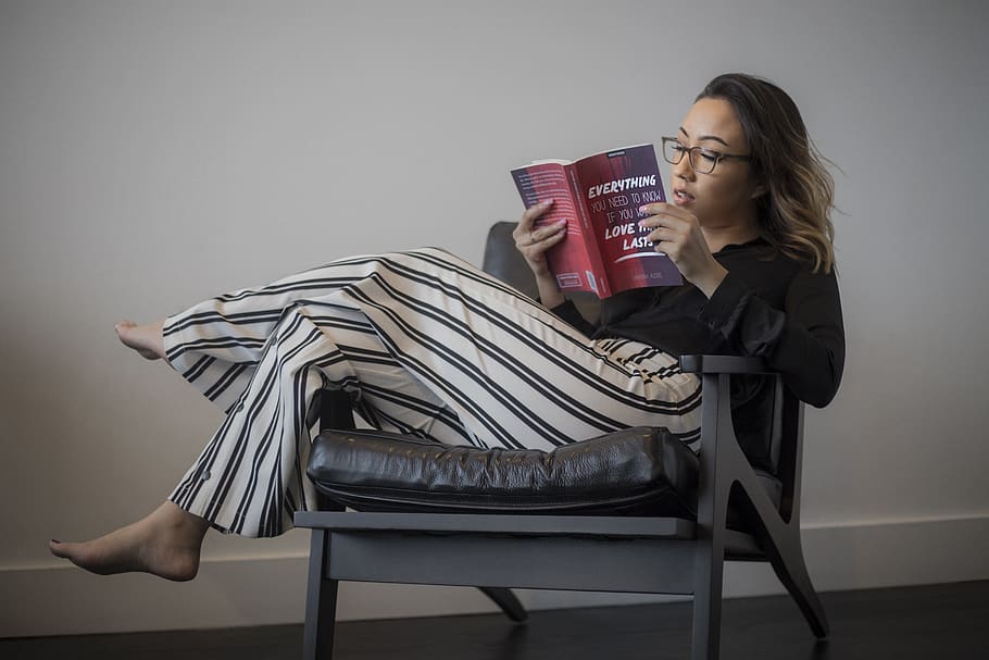 Women's Black Long-sleeved Top, White and Black Striped Pants Reading Book Sitting on Gray Wooden Framed Padded Armchair