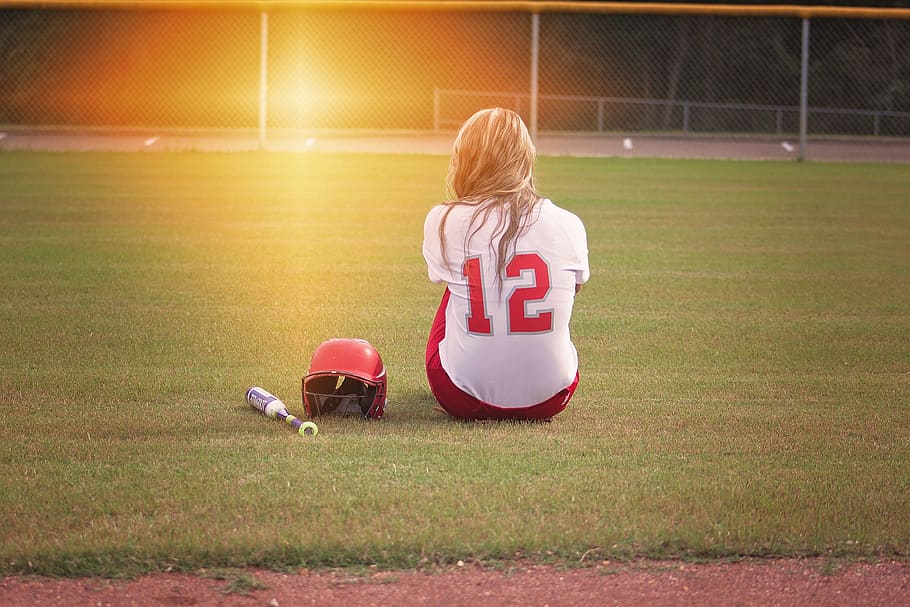Female Baseball Player Sitting on Grass Field Beside Helmet and Baseball Bat HD wallpaper