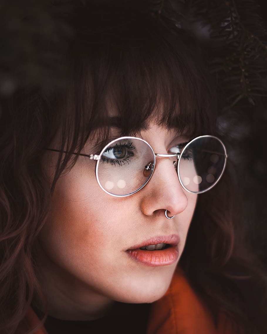 woman in orange top wearing round eyeglasses and nose ring, portrait