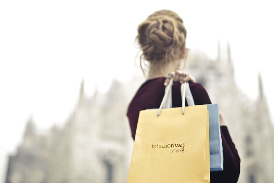 A young blond woman wearing a red velvet dress holding shopping bags in her hand on her shoulder