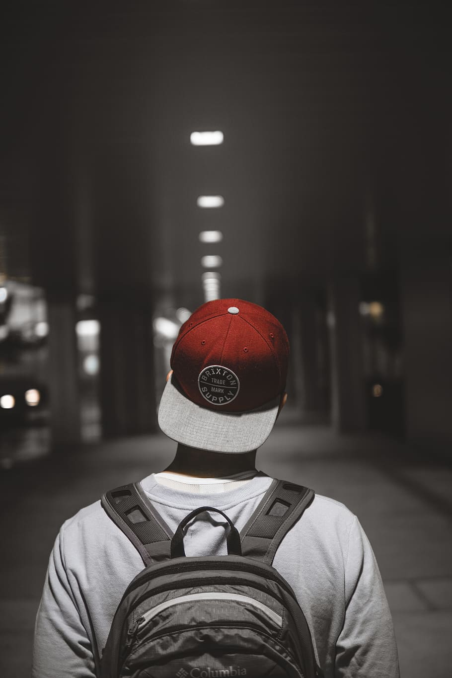 man wearing red cap facing the hallway, person, hat, backpack