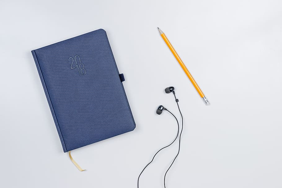 Pretty diary with a pencil and headphones on the white table. HD wallpaper