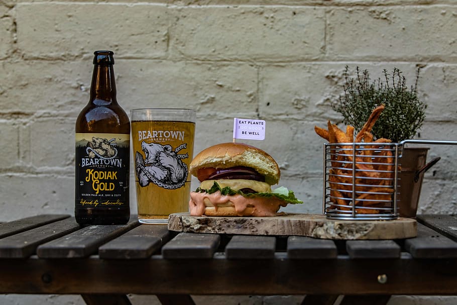 hamburger on chopping board by basket of fries and beer bottle