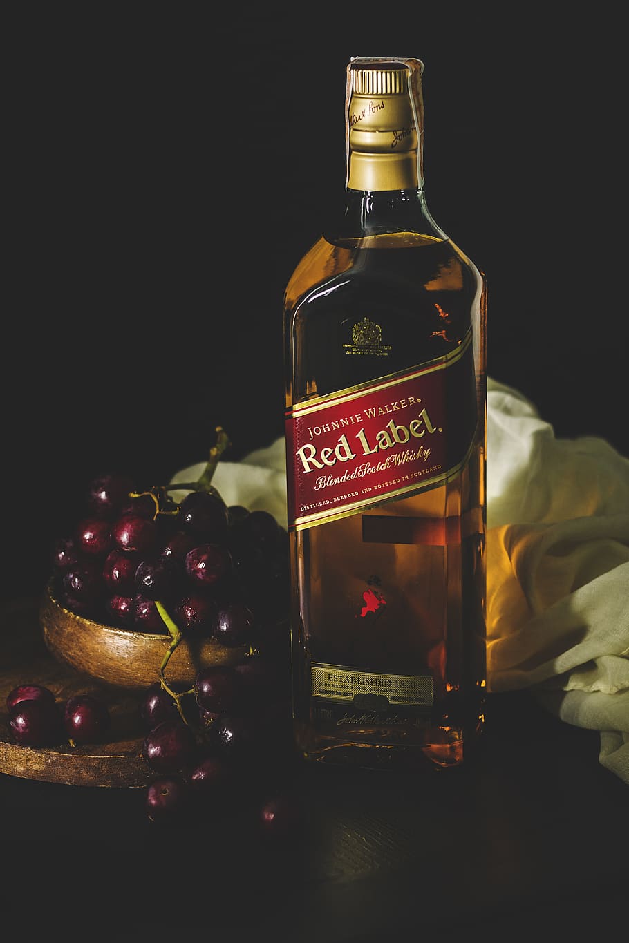 Johnnie Walker red label bottle beside bowl of red grapes, beverage
