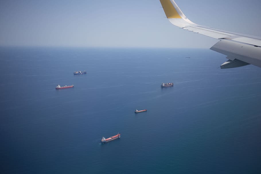 Aerial view of cargo ships in the ocean from the airplane window with aircraft wing in the fame