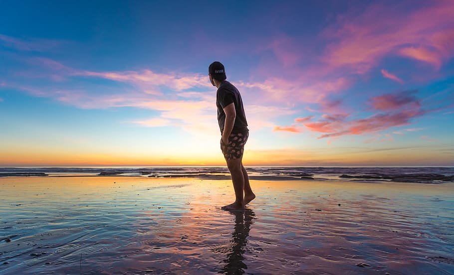 Man in Black T-shirt Wearing Cap Near Body of Water during Sunset HD wallpaper