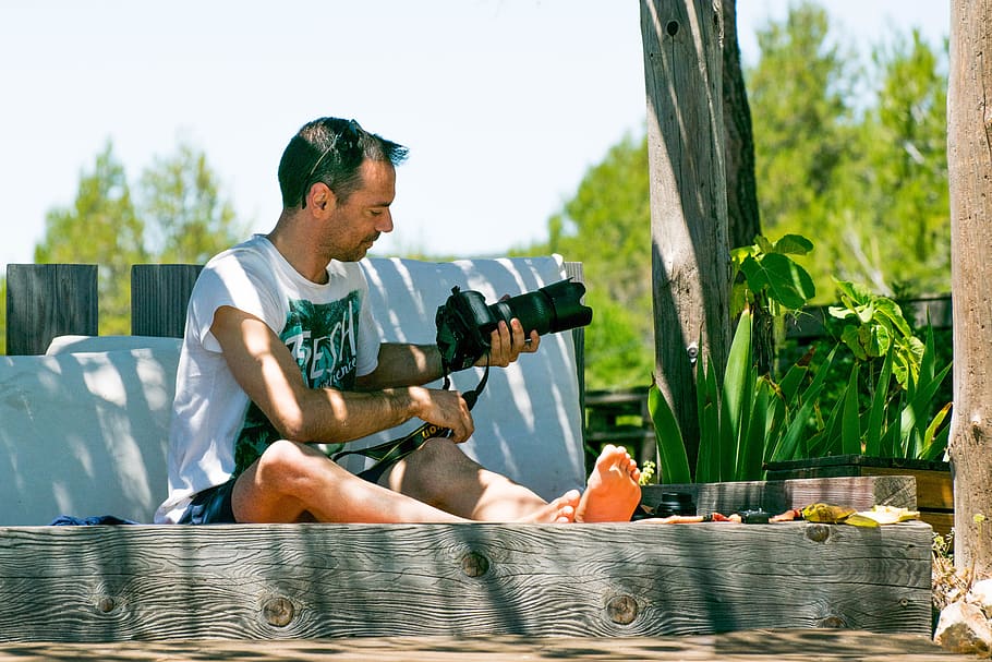 man sitting down while holding DSLR camera, person, human, gun HD wallpaper