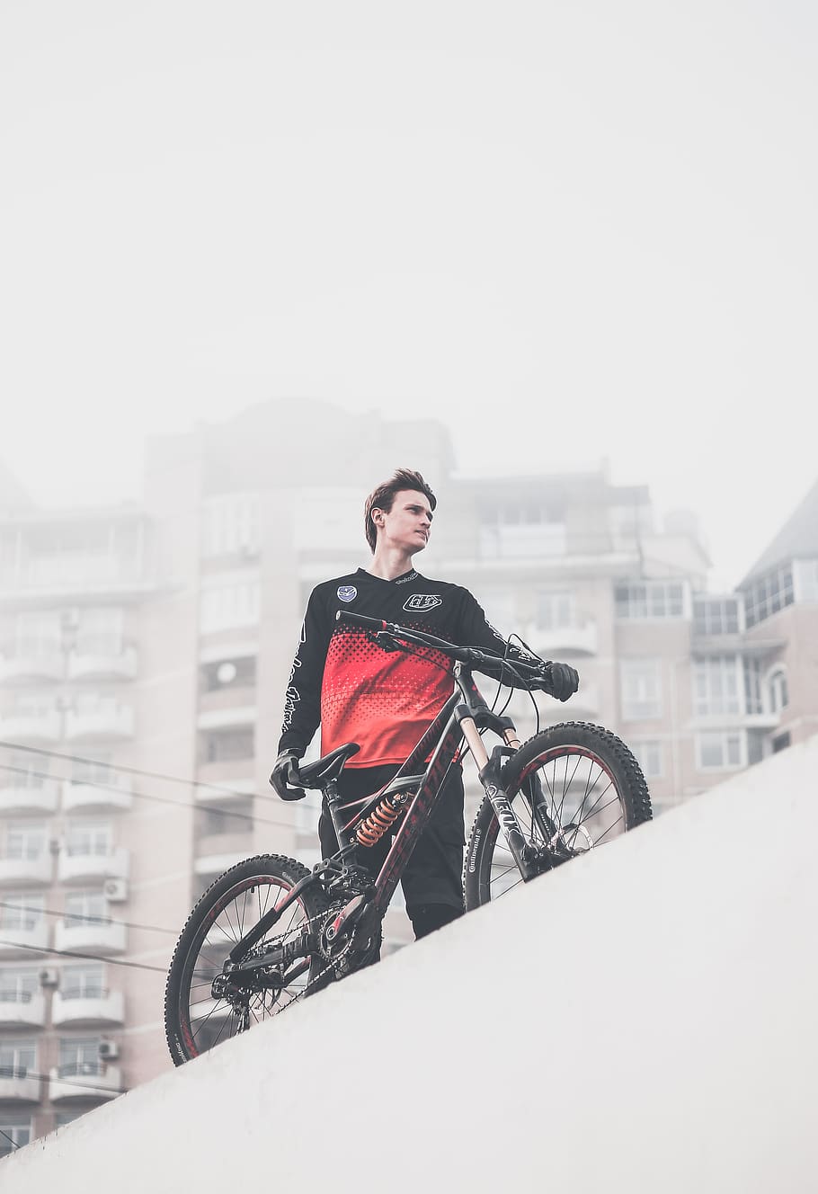 man wearing black and red ombre crew-neck long-sleeved shirt and black gloves standing on platform holding black full-suspension bike, HD wallpaper