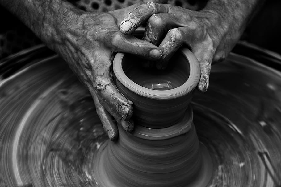 Messy hands sculpting on a pottery wheel in motion, human hand