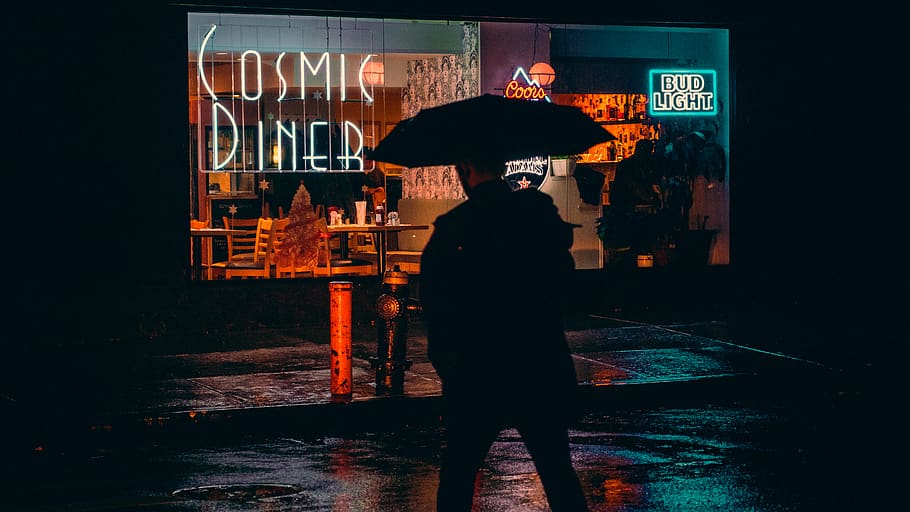 man under umbrella walking toward COsmic Diner building, human
