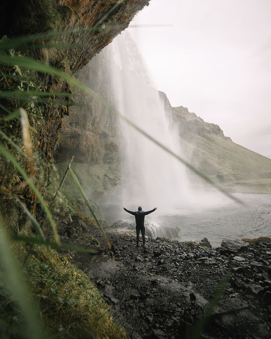 man raising two hands watching waterfall during daytime, reykjavík