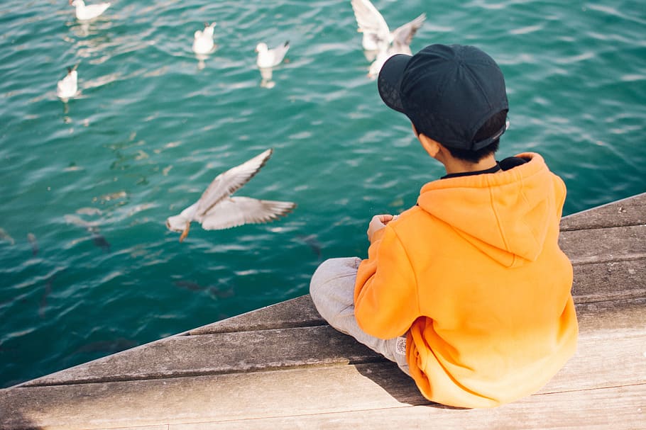 Boy Sitting Near Body of Water, alone, cap, child, daytime, hoody sweater, HD wallpaper