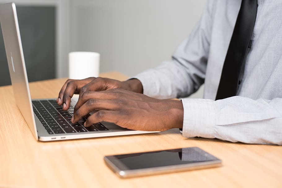 Person Wearing White Dress Shirt and Black Necktie Using Macbook Air on Beige Wooden Table HD wallpaper
