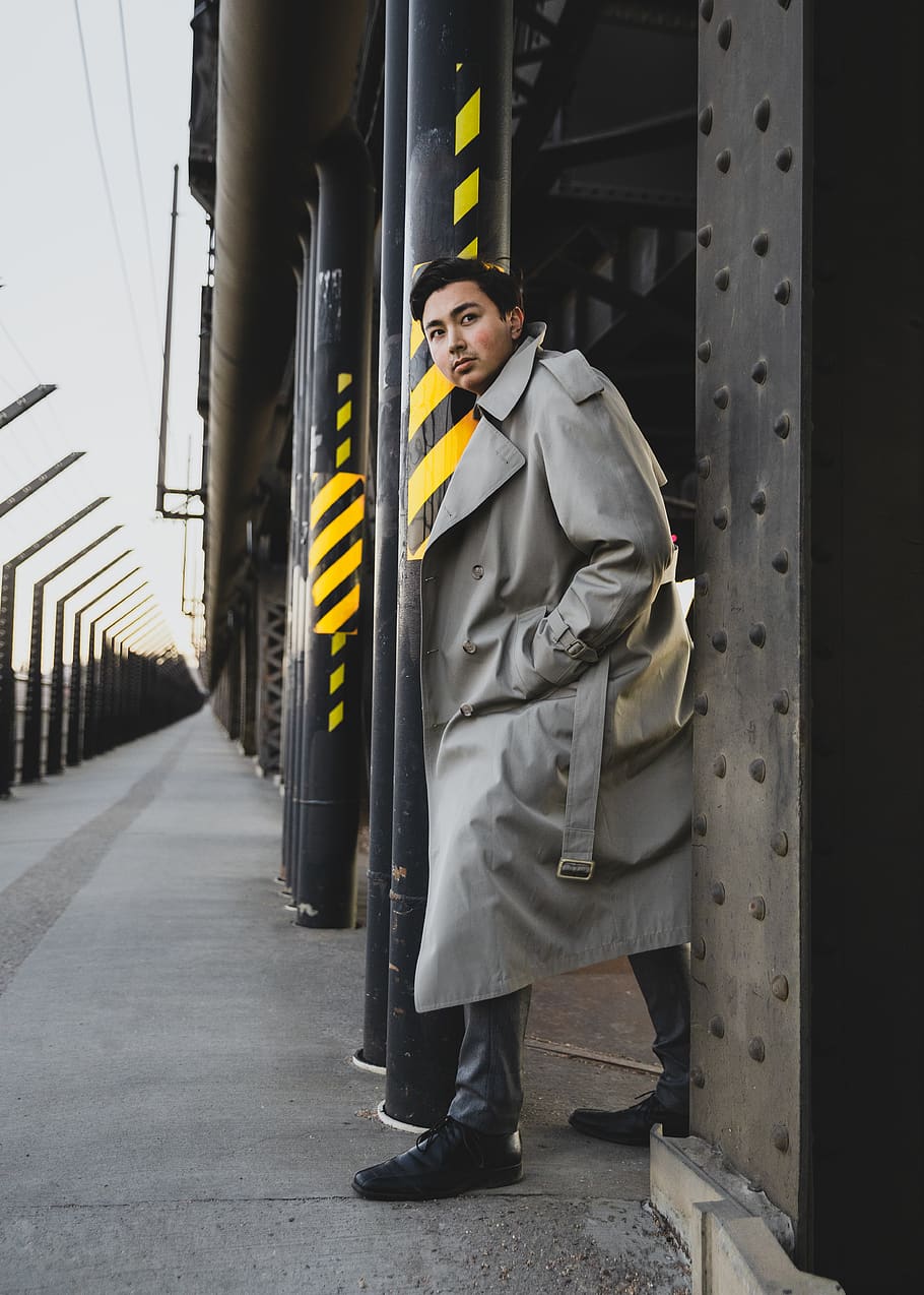 man in trench coat standing between poles, clothing, apparel