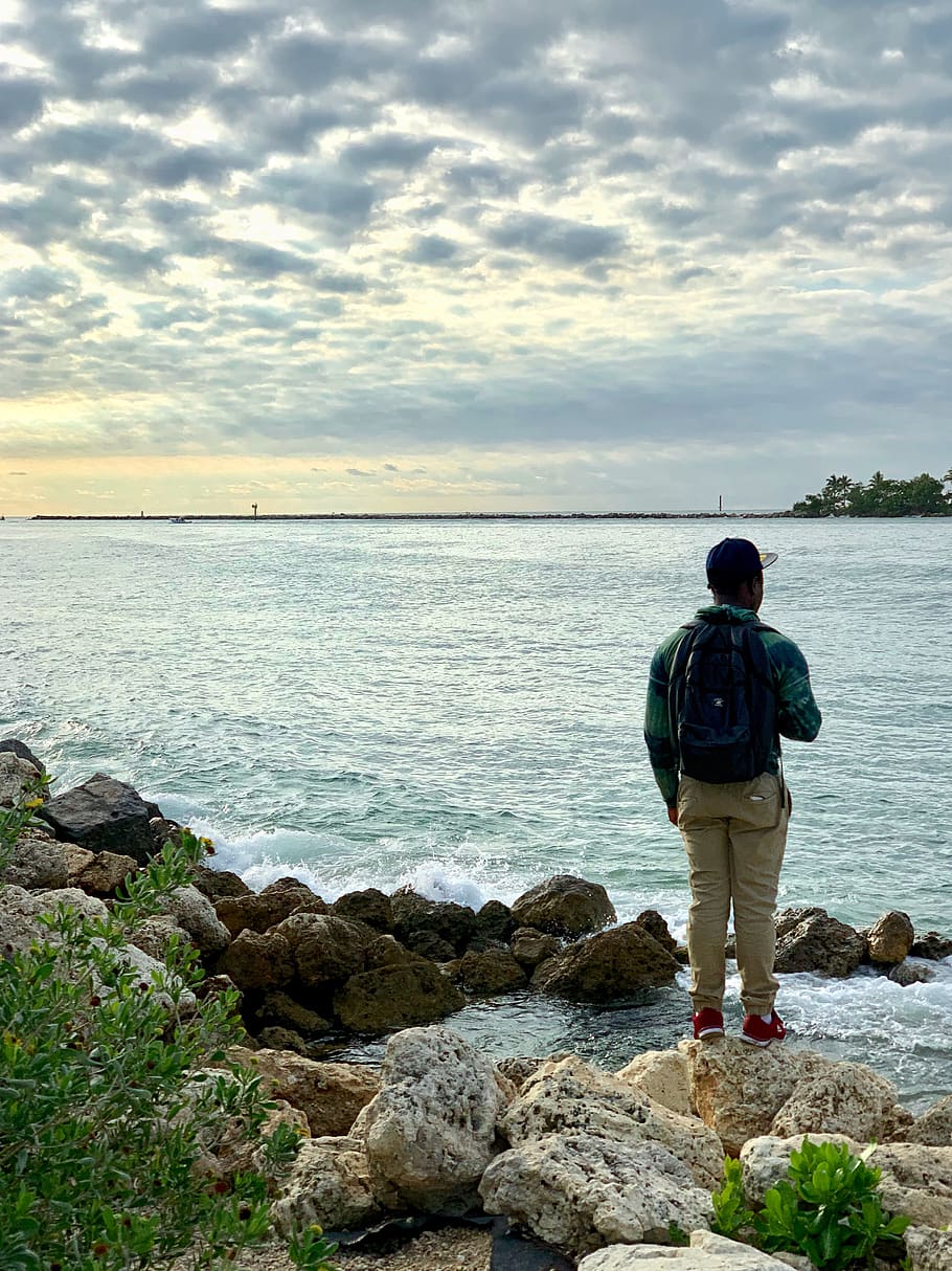 Man Standing on Rocks by the Water, adventure, backpack, cap HD wallpaper