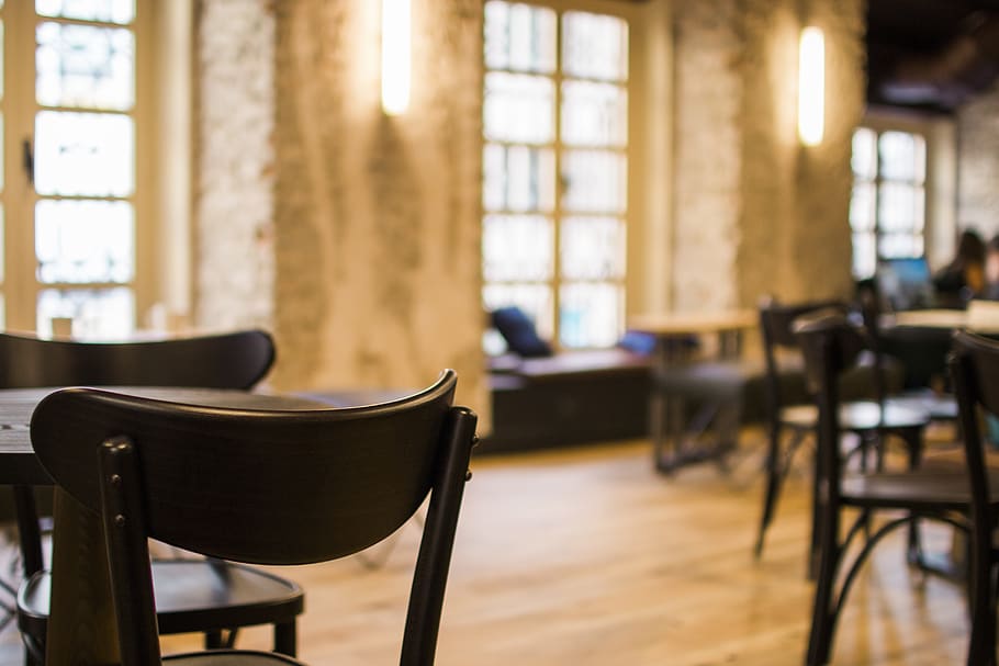 Black Wooden Tables and Chairs Arranged Inside Restaurant With Yellow Sconce HD wallpaper