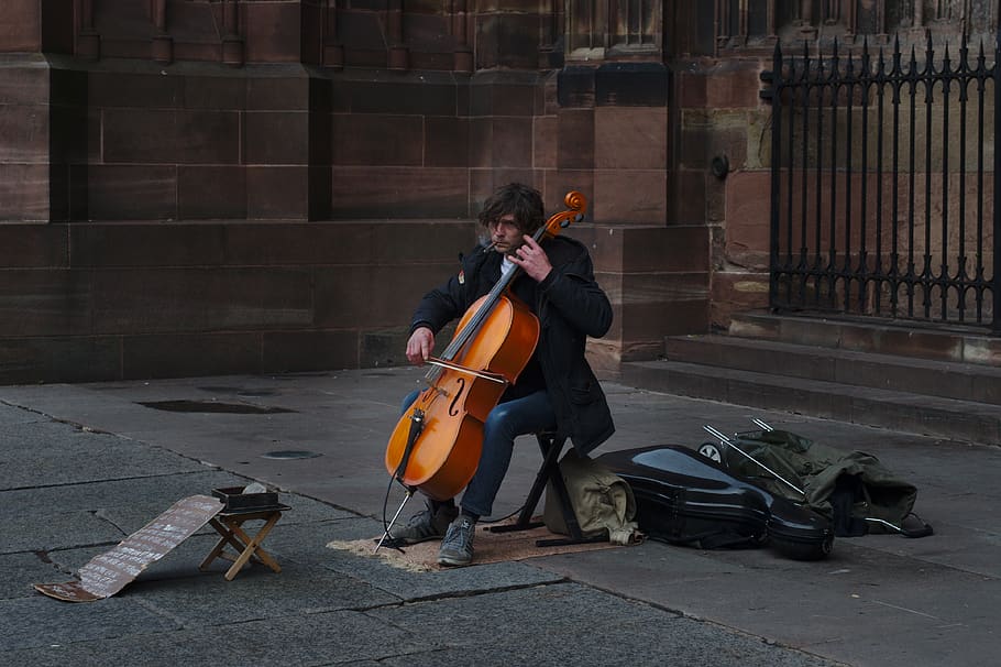 man playing cello near black gate, musician, person, human, musical instrument