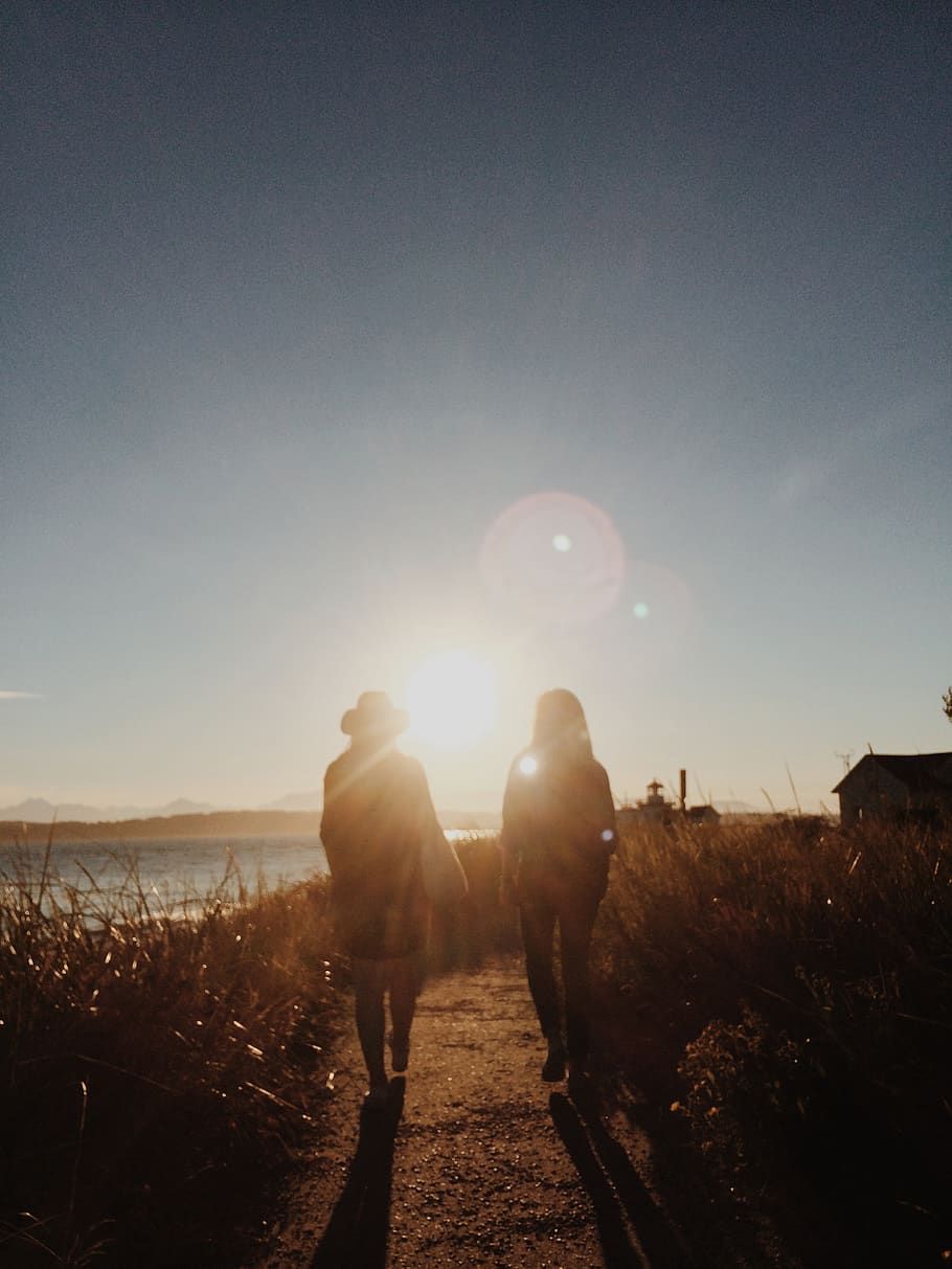 Silhouette of Two People Walking Near Body of Water during Golden Hour HD wallpaper