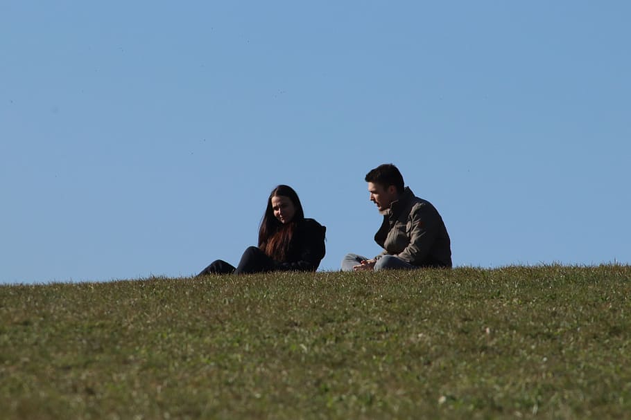 man and woman sitting on green grass field during daytime, plant