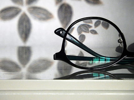 Abstract view of a pair of black rimmed glasses against a floral pattern background with a turquoise light reflection in the lense HD wallpaper