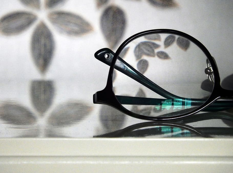 Abstract view of a pair of black rimmed glasses against a floral pattern background with a turquoise light reflection in the lense HD wallpaper
