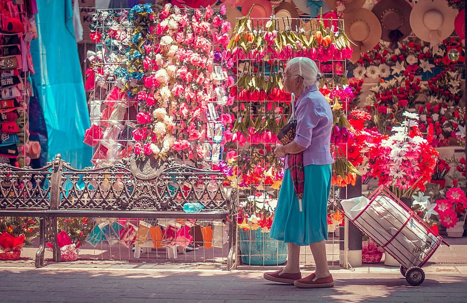 An older Asian woman with white hair pulling her cart along a flower vendor.