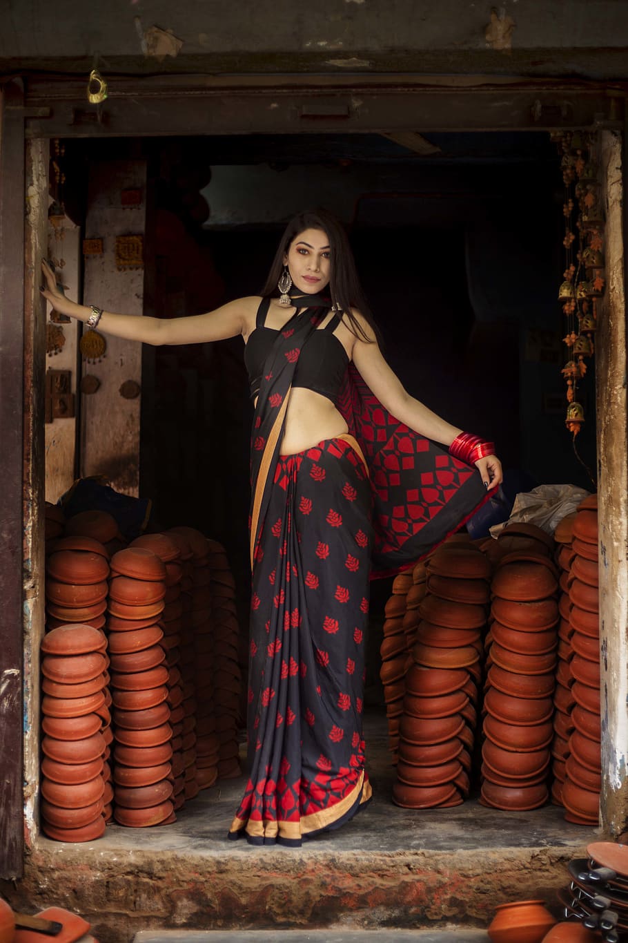 woman wearing red and black saree dress standing near brown clay pots