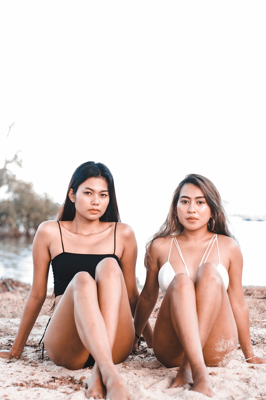 two women wearing bikinis while sitting on shoreline, young women