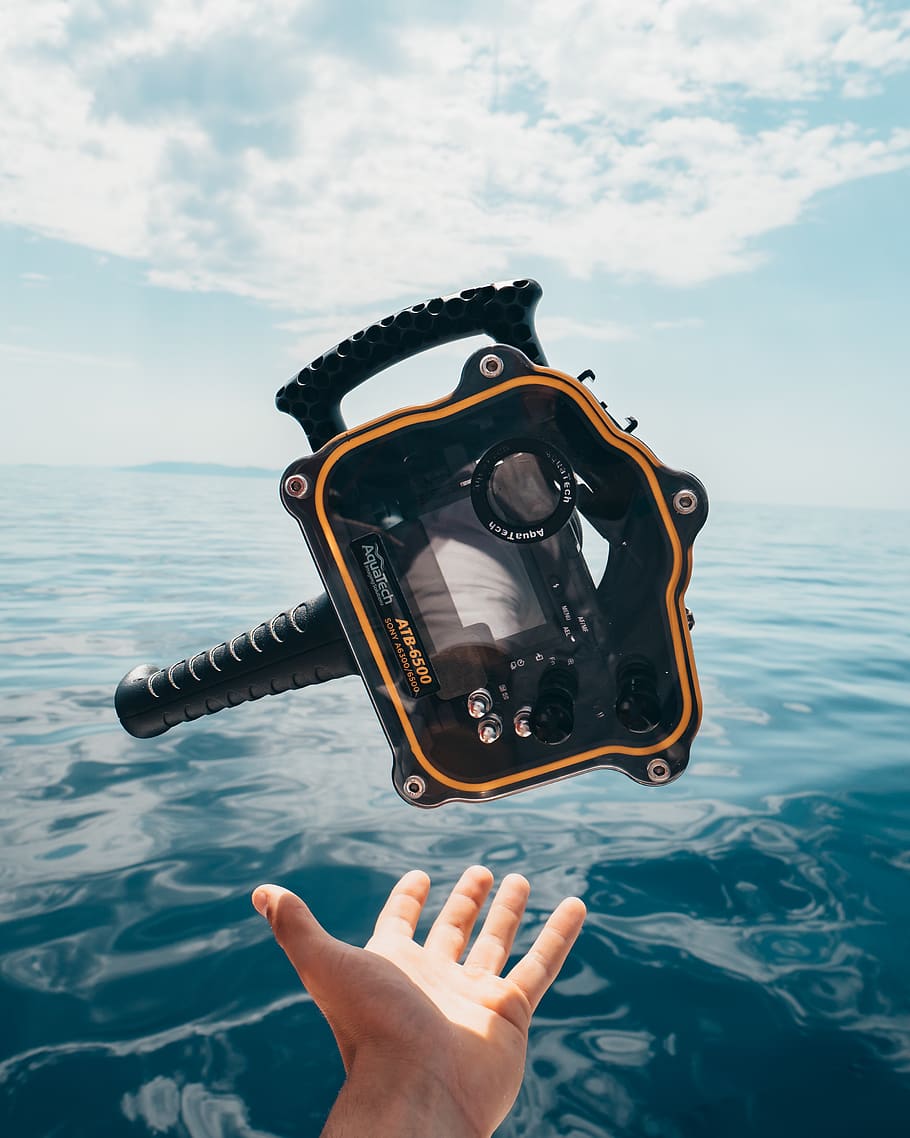 Person Grabbing Black and Orange Plastic Case Front of Calm Water HD wallpaper