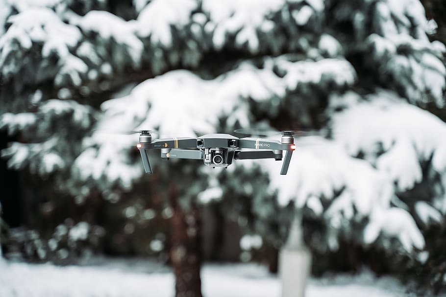 flying gray quadcopter drone near snowcovered trees, pine, winter