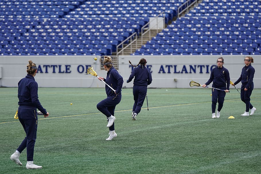 women playing lacrosse on green field during daytime, person