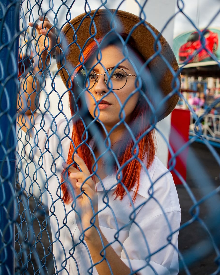 Woman Wearing White Collared Top and Beige Hat Behind of Blue Cyclone Fence