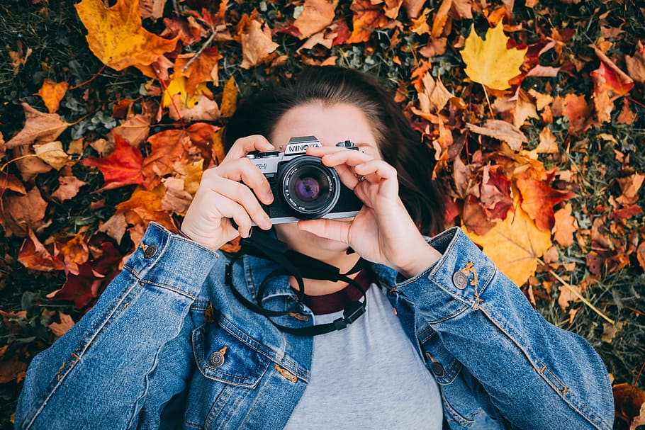 woman laying on maple leaves using black Minolta DSLR camera HD wallpaper