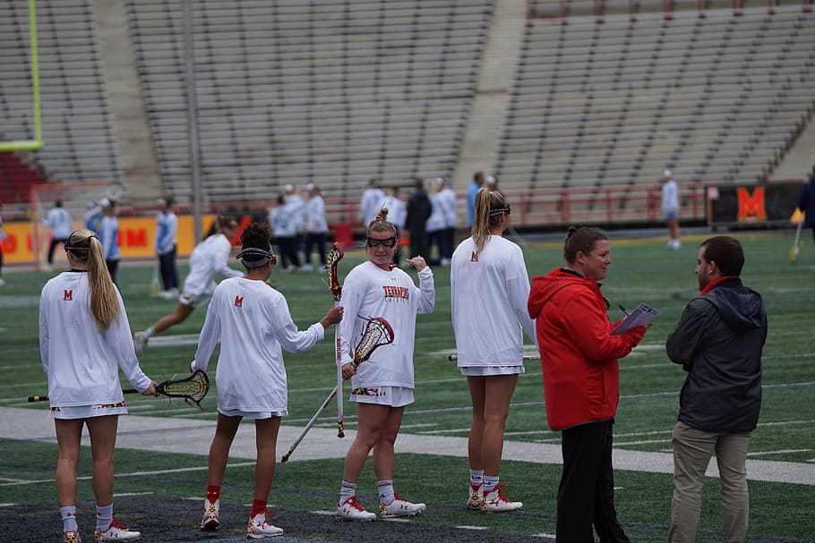 four women holding lacrosse stick standing on field, person, human