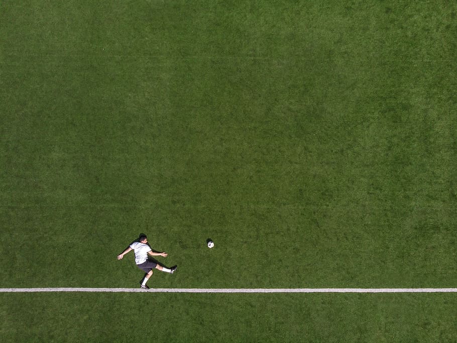 Aerial view of a striker lying down on the field in a position as if he has kicked the football place away from him