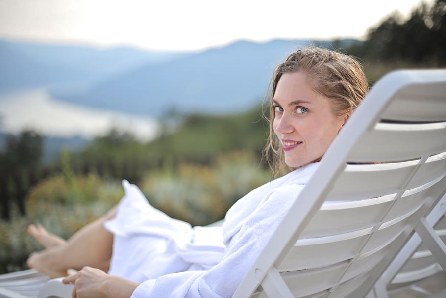 Selective Focus Photography of Smiling Woman Wearing White Bathrobe Lying on Pool Chair