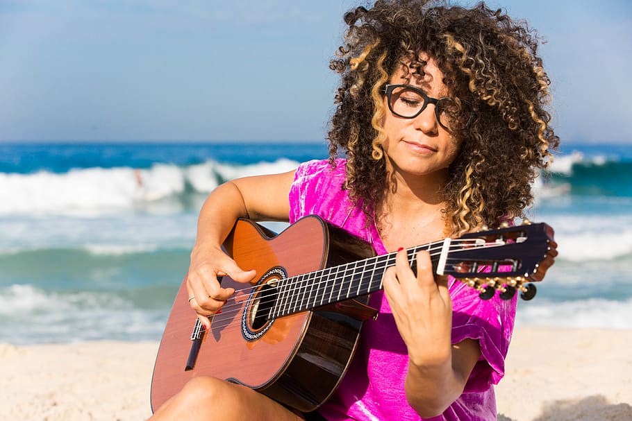 Woman Wearing Purple Shirt Playing Brown Classical Guitar While Sitting Near Shoreline With Water Splashing Background in Daytime HD wallpaper