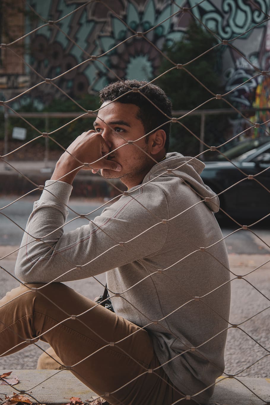 man sitting beside fence with hand on face outdoors during daytime HD wallpaper