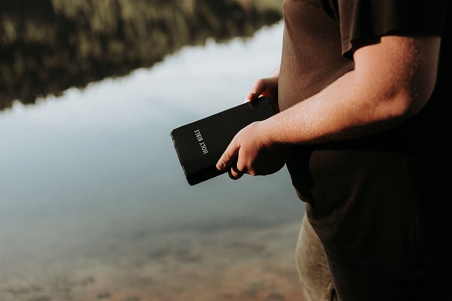 black Holy Bible, one person, hand, human hand, water, lake, focus on foreground HD wallpaper