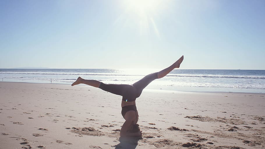 A woman stretching her legs in handstand position on the beach.