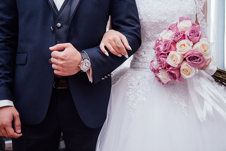A bride holding a pink and white roses bouquet while holding arms with her husband.
