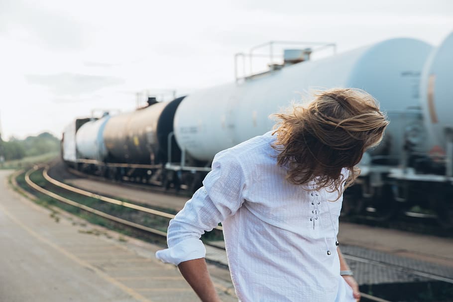 A long haired young caucasian man standing near passing train