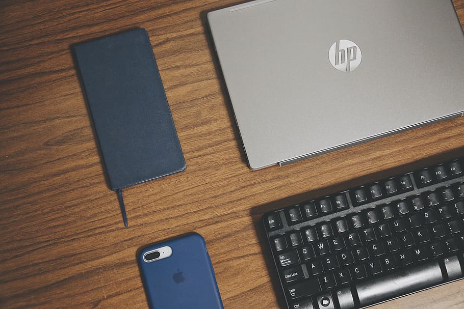 gray HP laptop, smartphone, and keyboard on brown surface, hardware