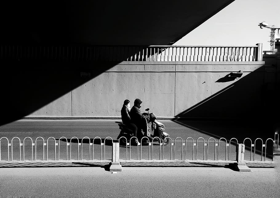 grayscale photo of two person sitting near fence, handrail, banister