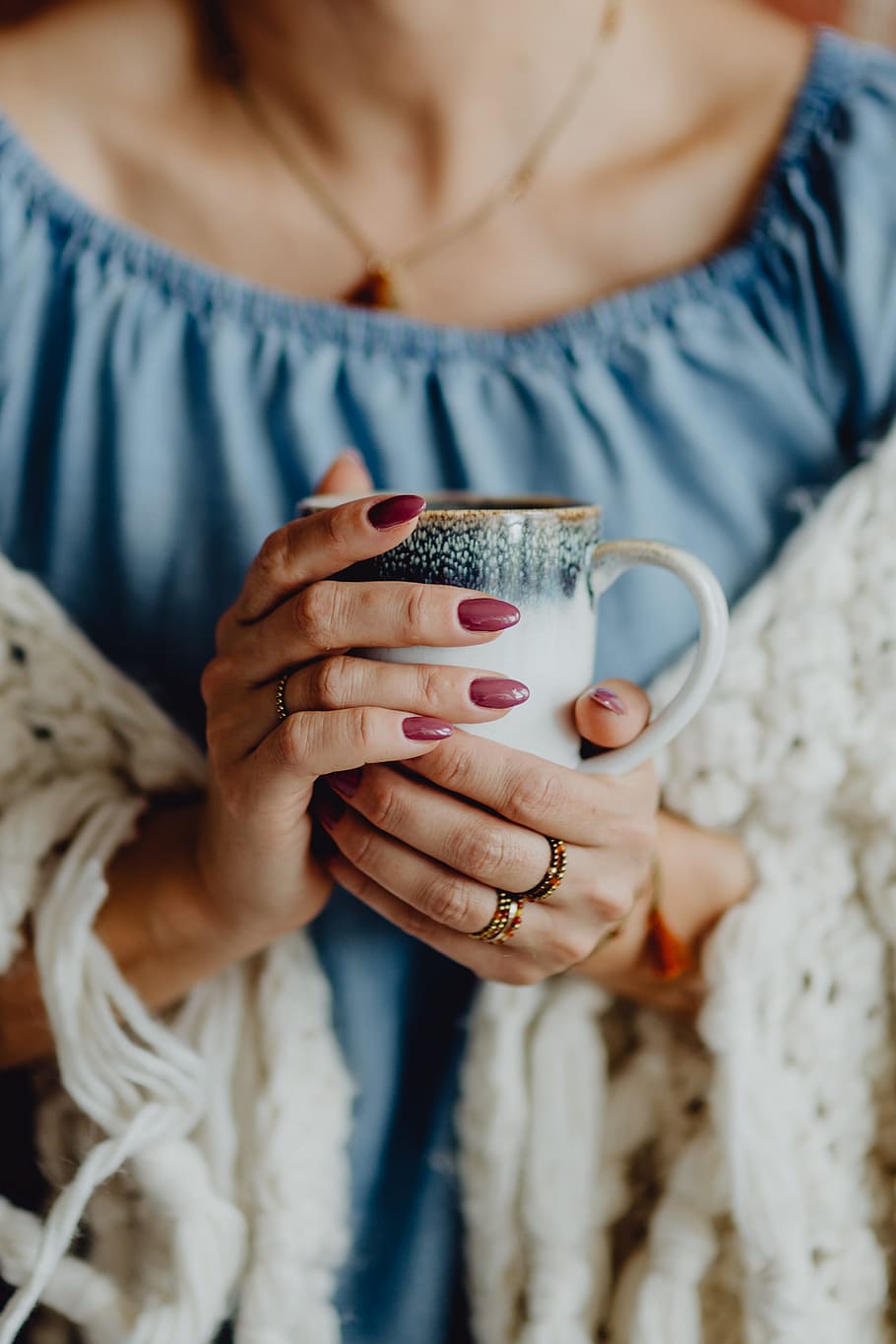 A woman in a warm blanket holds a cup of coffee or tea, cup of tea