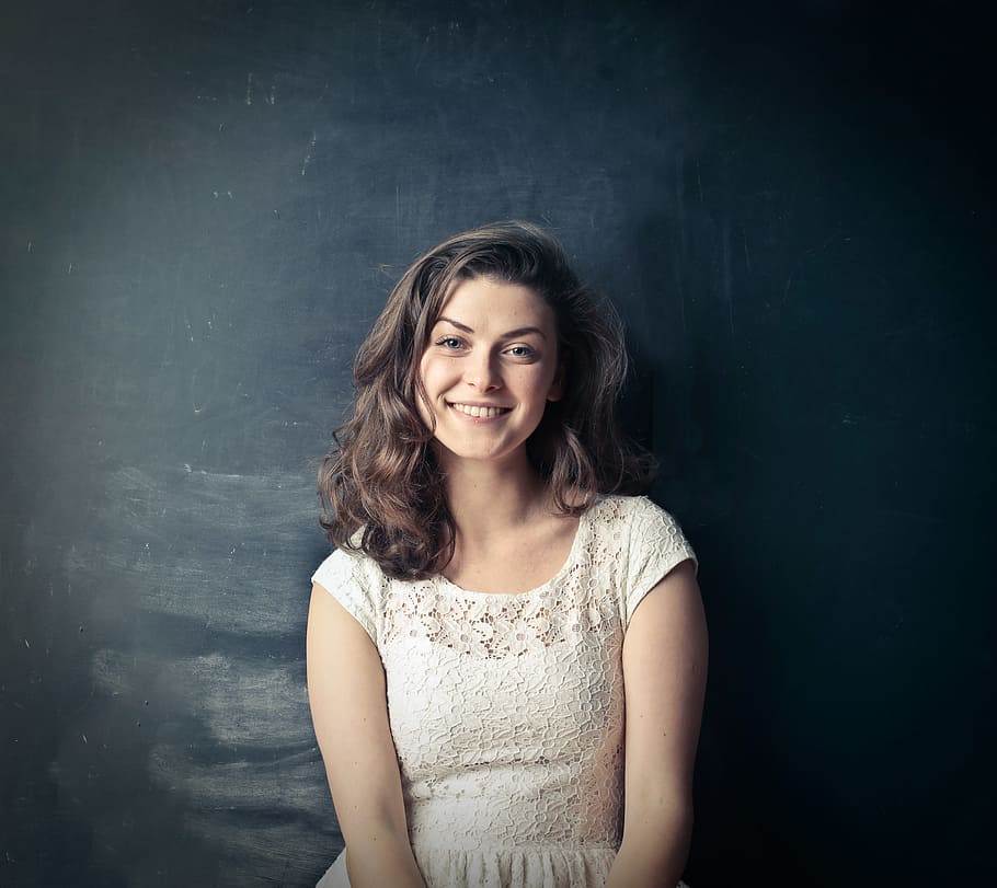 Brown Haired Woman In White Sleeveless Dress Smiling While Standing Against Blackboard with erasure marks, HD wallpaper