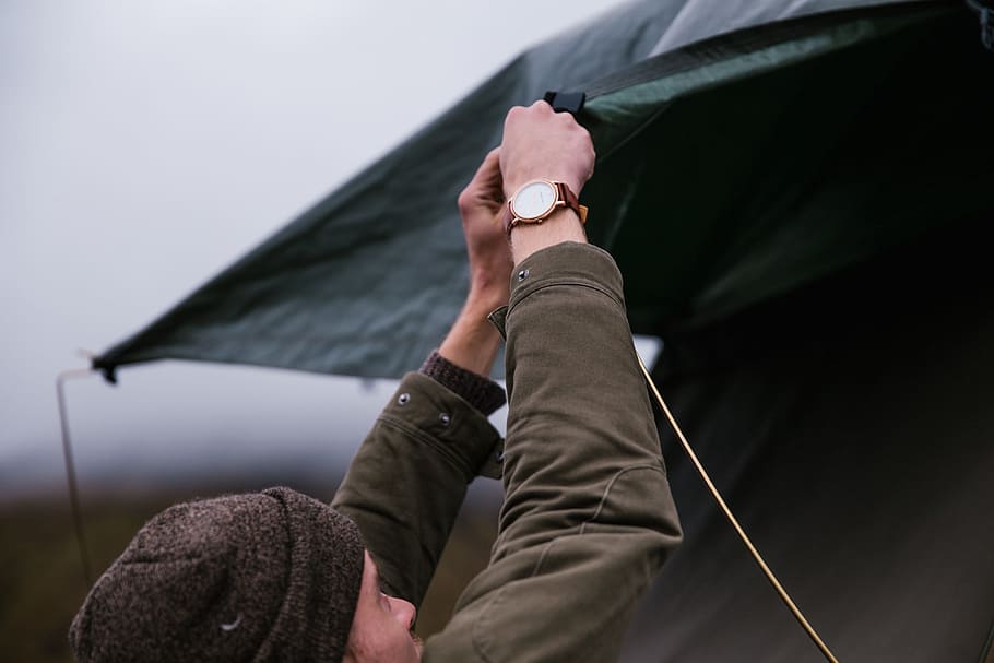 A young caucasian man wearing brown jacket setting up tent, 25-30 year old