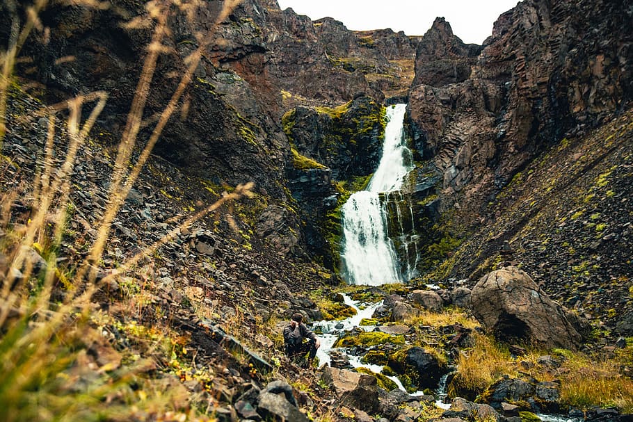 A hiker resting on a rock by the glacier waterfall in the mountains, HD wallpaper