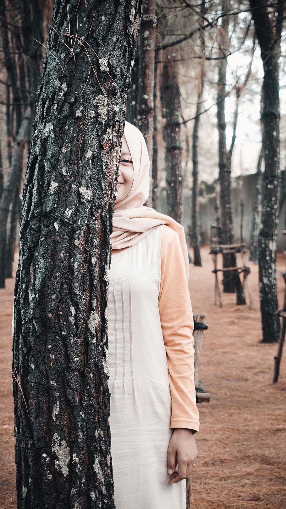 smiling woman standing and hiding half face on tall tree, clothing