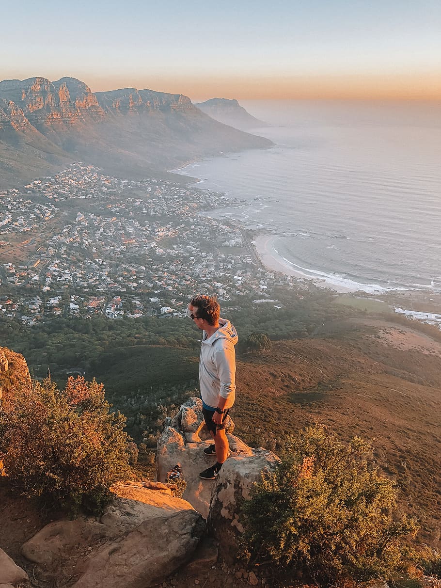 man standing on ledge overlooking town, cape town, lions head